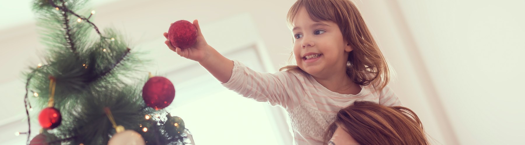 Mother with daughter on shoulders decorating a christmas tree