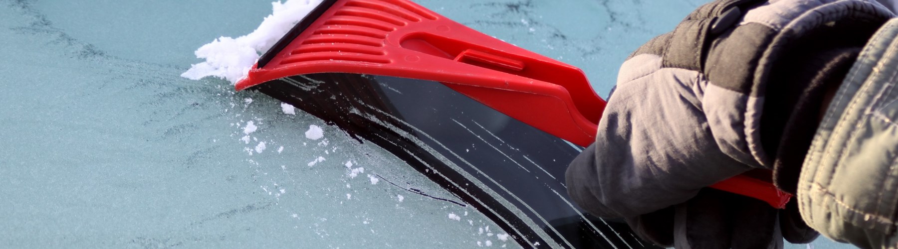 Red ice scraper scraping ice on car windscreen