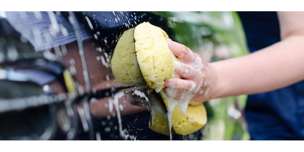 Woman's hand washing car with a yellow sponge