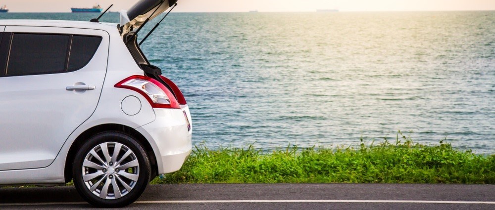 White hatchback car parked on a beach road with boot open
