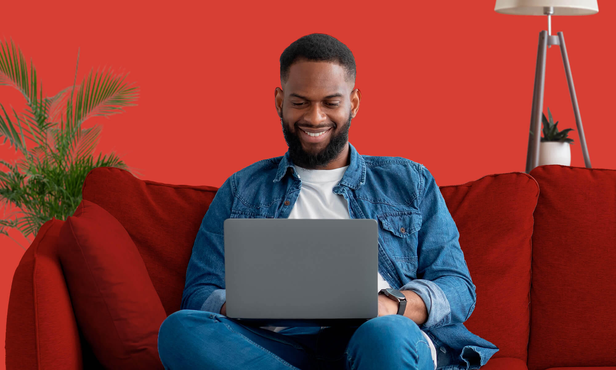 Man sits on red sofa with laptop and red background